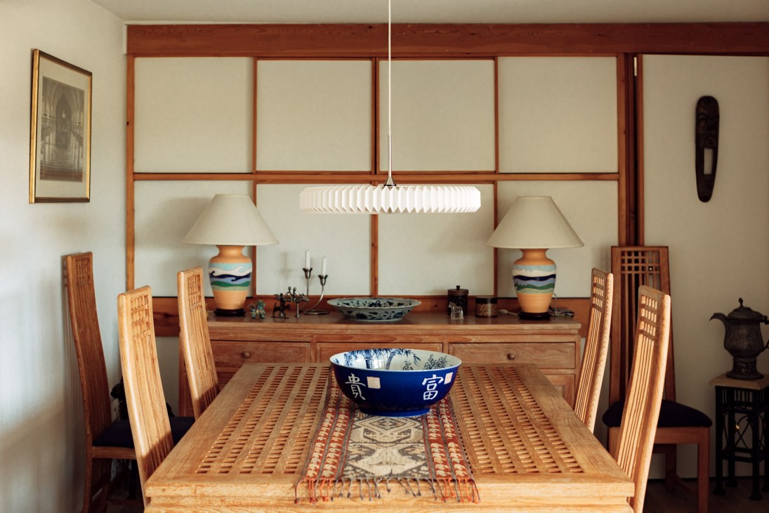 Dining area with wooden table and chairs, pendant light, ceramic bowls, and sliding hatches leading to kitchen.