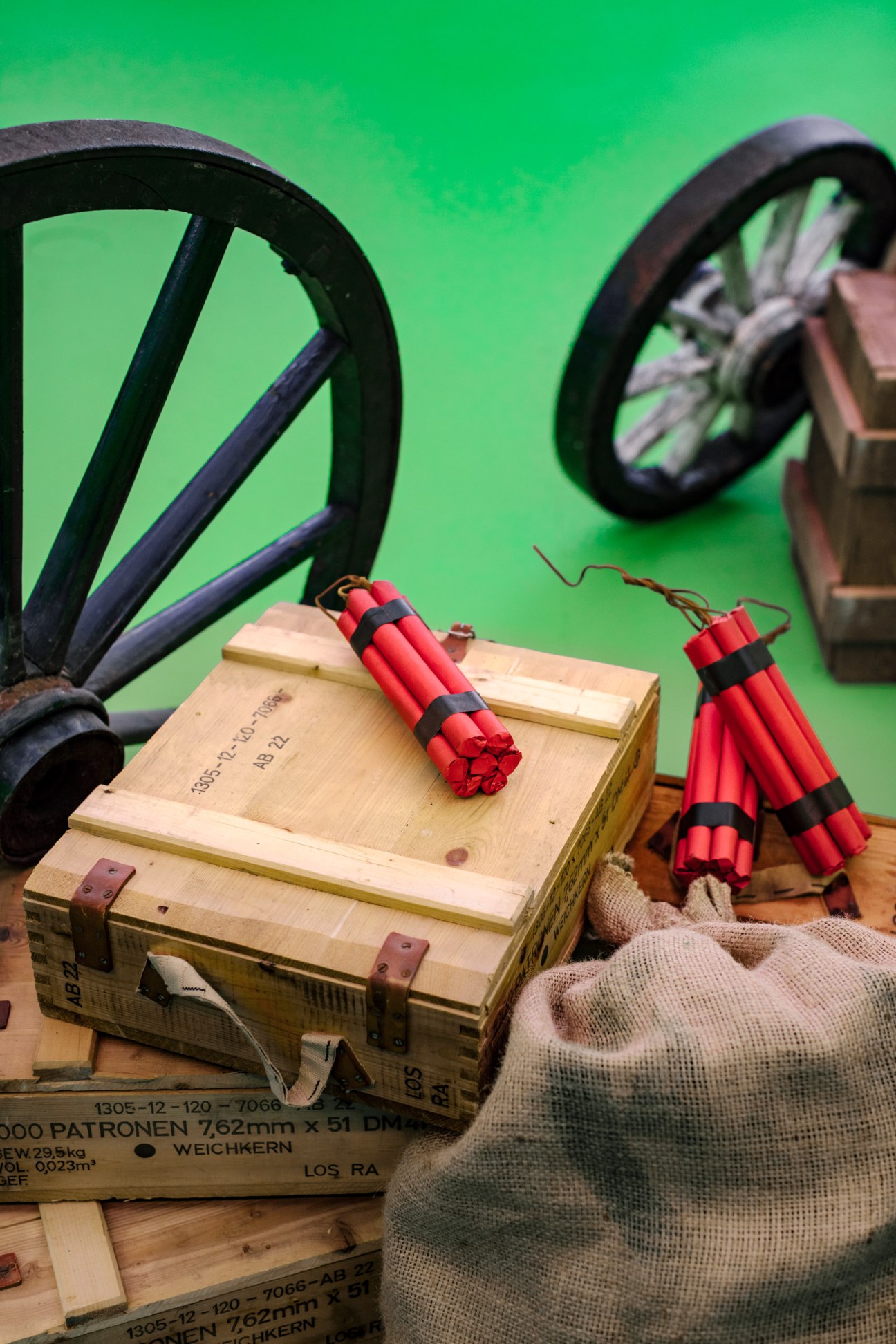 Studio props for Lost in Time game show including wooden crates, red dynamite bundles, and wagon wheels against a green screen.
