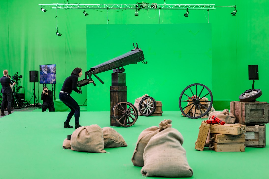 Woman aiming a cannon on a green screen set with western props while crew films the interactive game show Lost in Time.