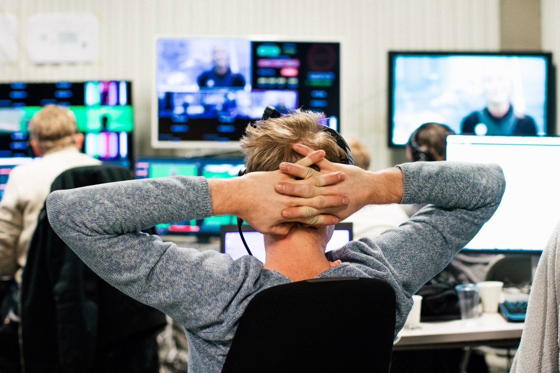 Person relaxing with hands behind head in control room with multiple screens showing Lost in Time graphics.
