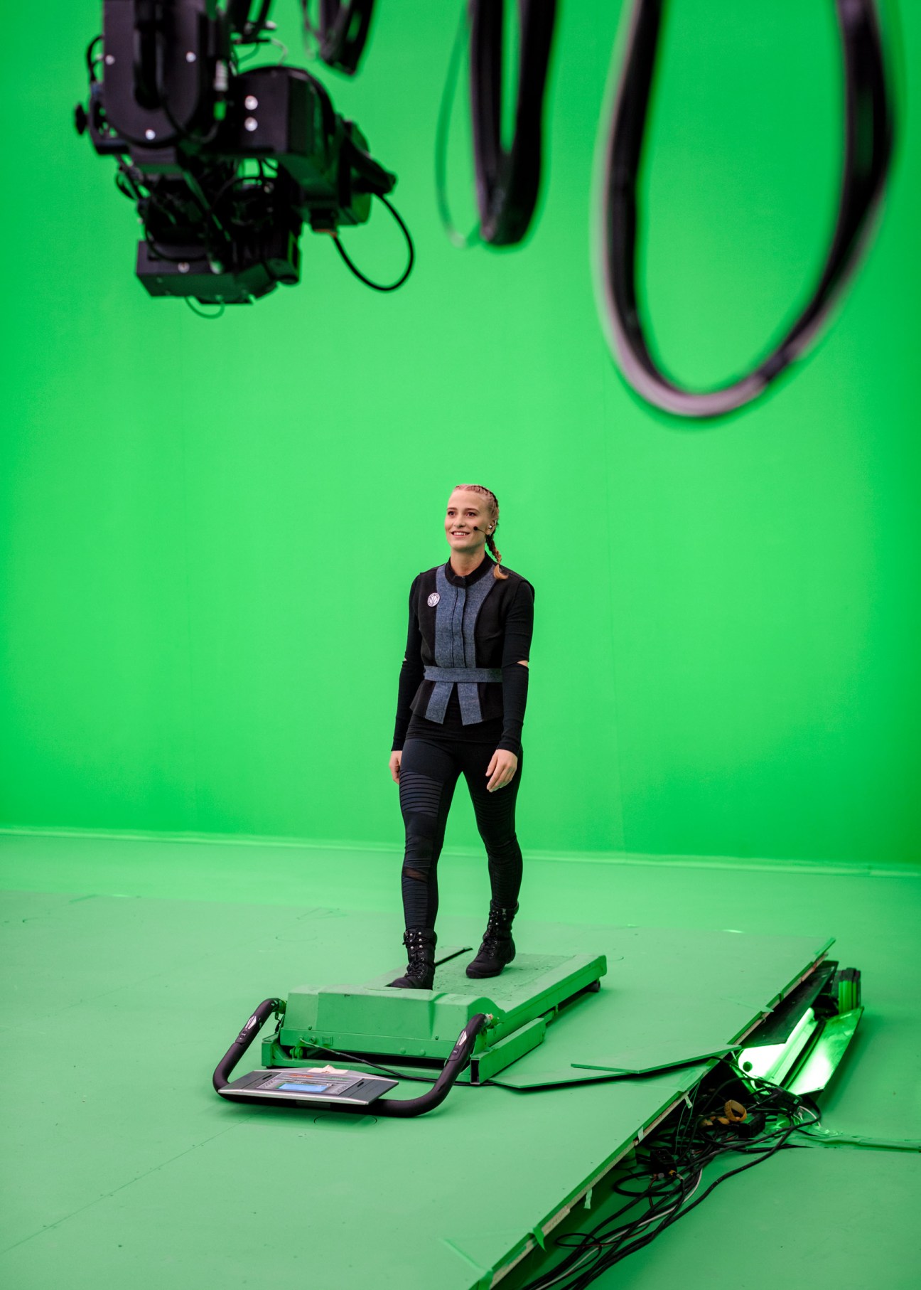 Woman standing on a green treadmill against a bright green screen in a studio.
