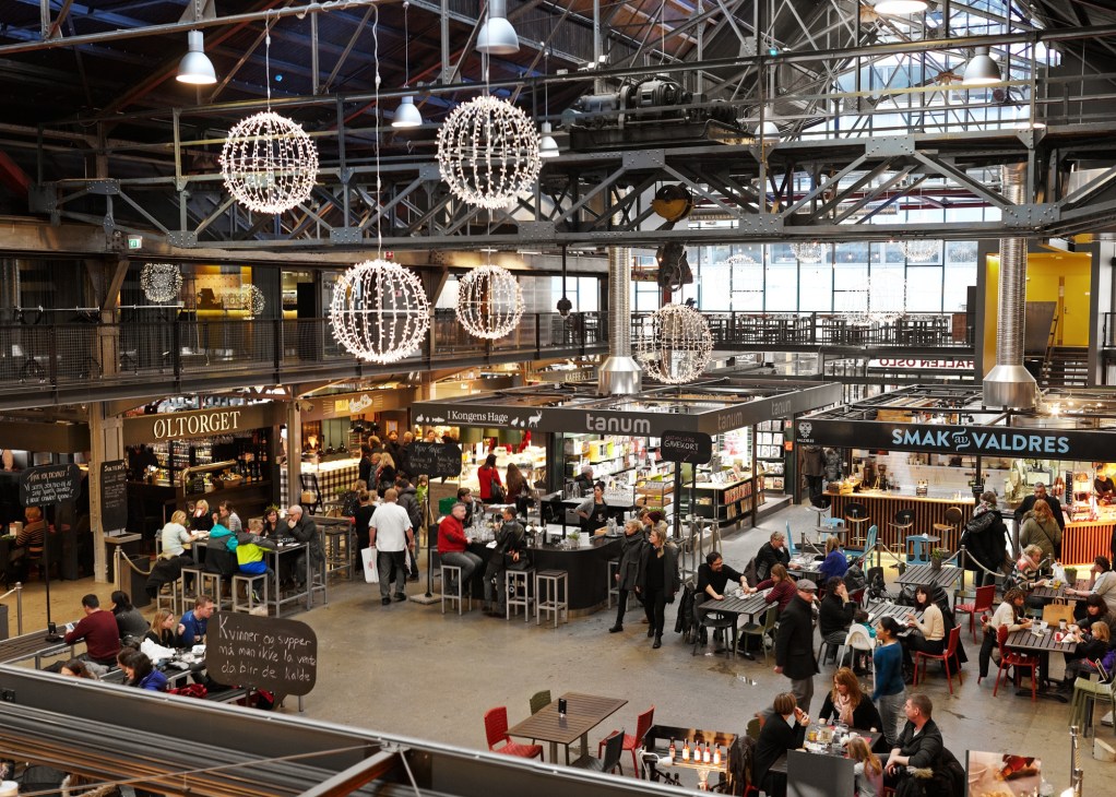 Interior view of Mathallen food hall with multiple vendor stalls, hanging sphere lights, and diners at communal tables.