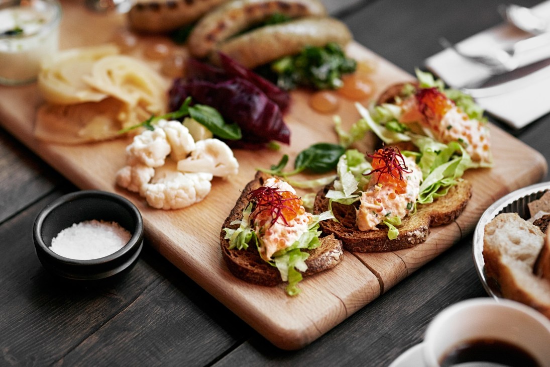 Nordic-inspired appetizers on wooden board at Von Porat restaurant, featuring open-faced sandwiches with seafood and fresh garnishes.