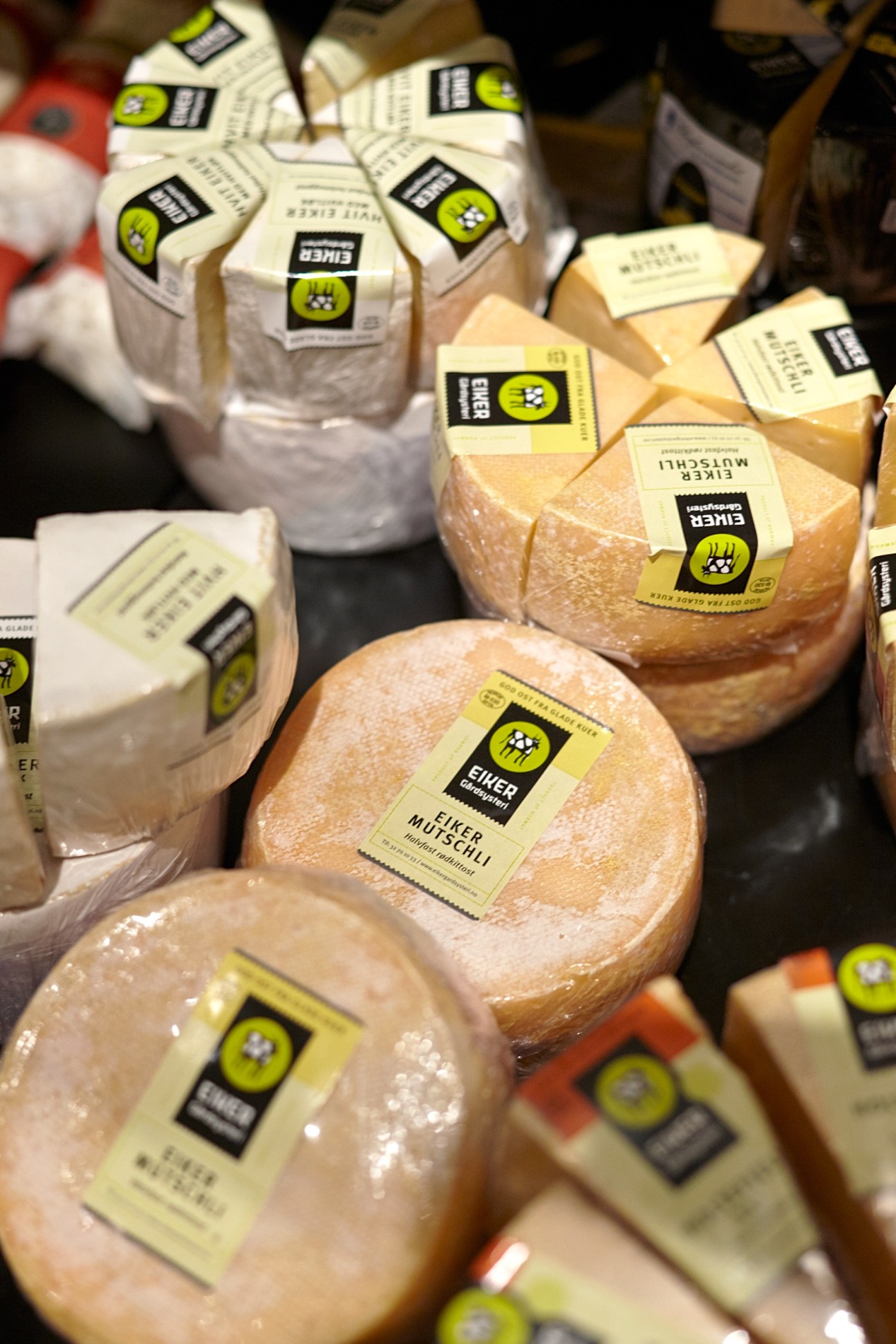 Wrapped cheese wheels and blocks with yellow and black labels at Melkerampa dairy shop.