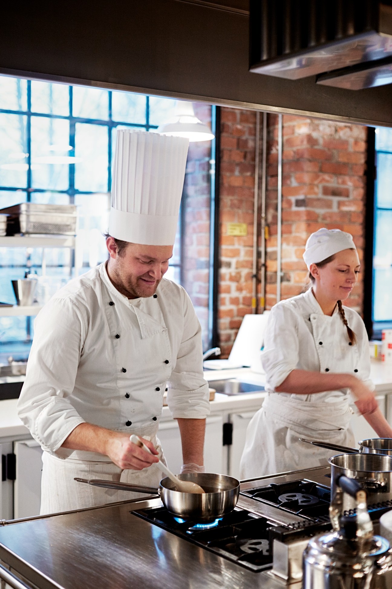 Two chefs in white uniforms and chef's hats cooking at Melkerampa in Mathallen food hall.