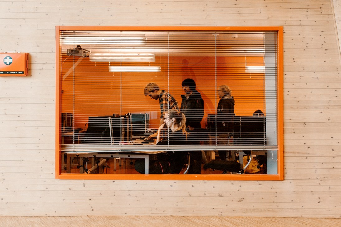 Students visible through internal windows with orange frame in wooden interior of University Centre in Svalbard.