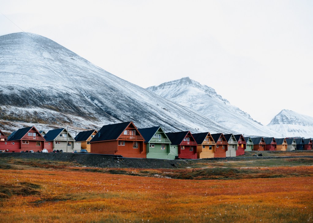 Colorful terraced houses in Longyearbyen with snow-covered mountains in the background.