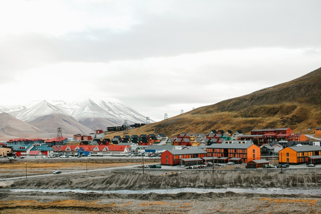 Panoramic view of Longyearbyen's colorful waterfront buildings with snow-capped mountains in the background.