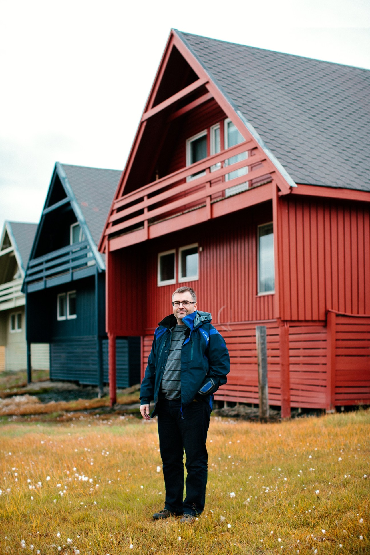 Man standing outside red pitched-roof house with blue house visible behind in Longyearbyen