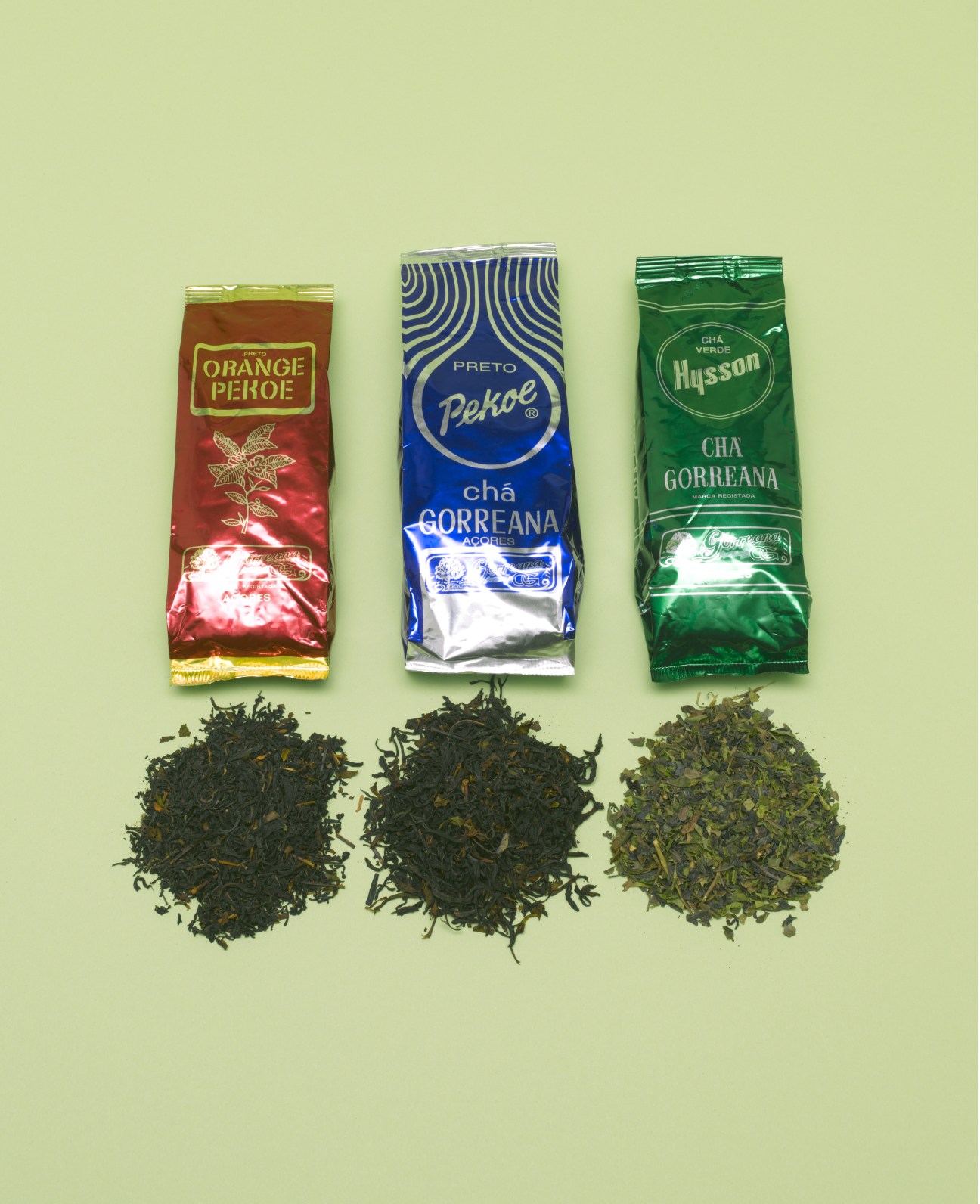 Three Chá Gorreana tea packets with loose tea leaves displayed below on a pale green background.