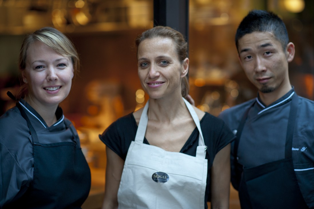 Three staff members smiling at NoGlu restaurant in Paris, wearing black and white uniforms.