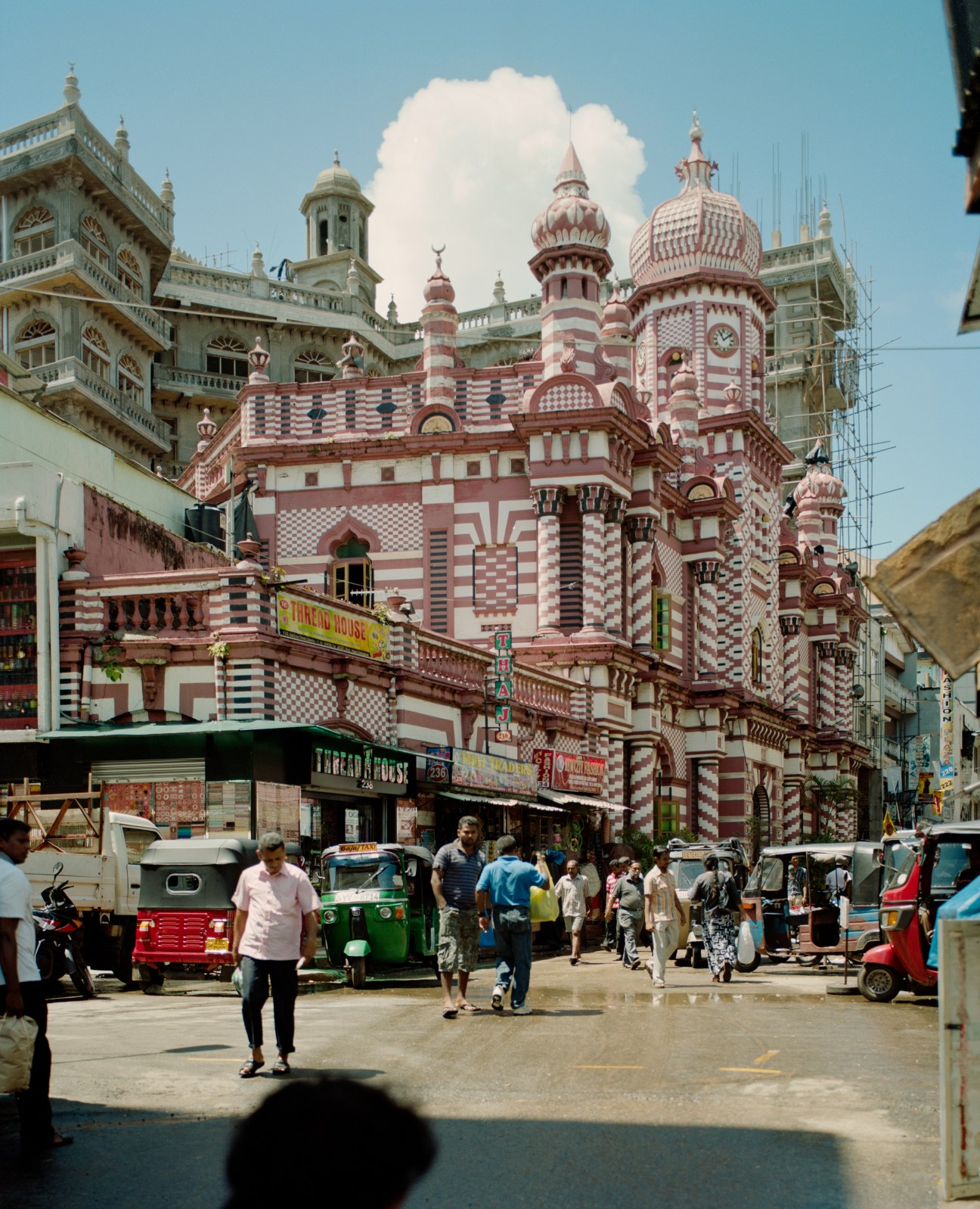 A vibrant red and white striped Hindu temple with ornate domes and spires surrounded by street vendors and trishaws in Colombo.