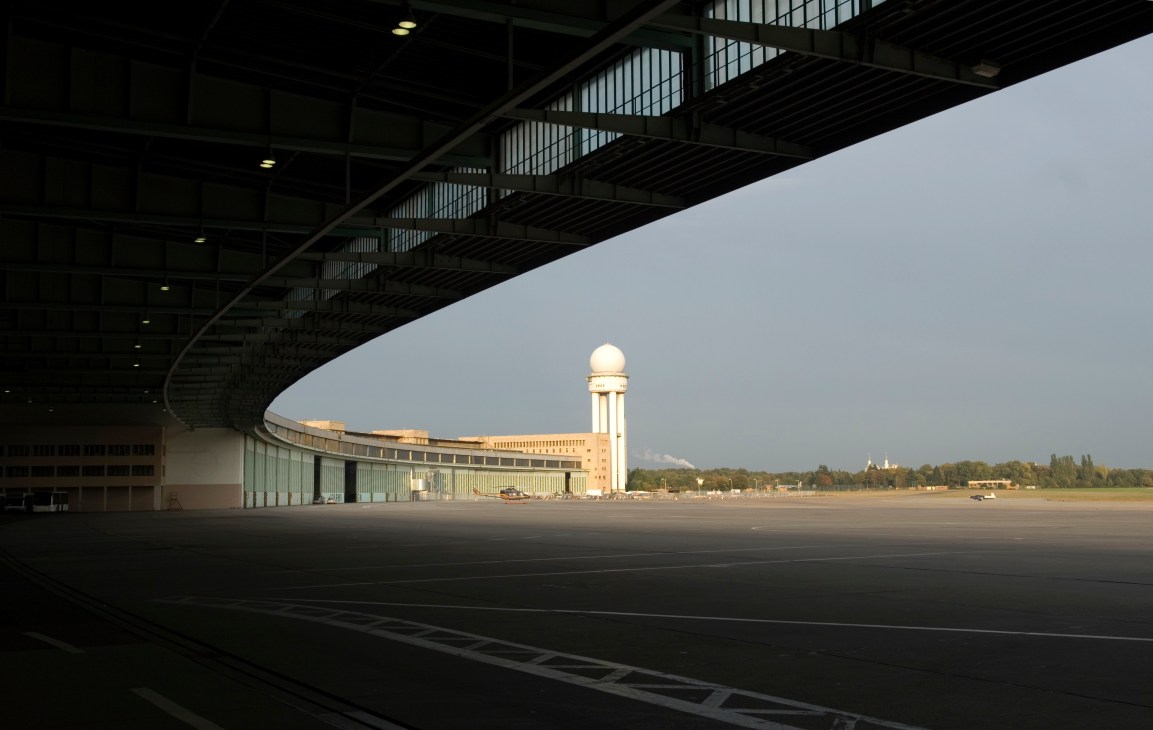 Tempelhof airport's radar tower visible in the distance across an empty runway, viewed from under a curved hangar structure.