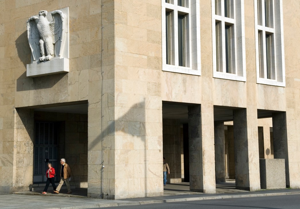 Stone eagle sculpture mounted on beige stone building facade with people walking below.