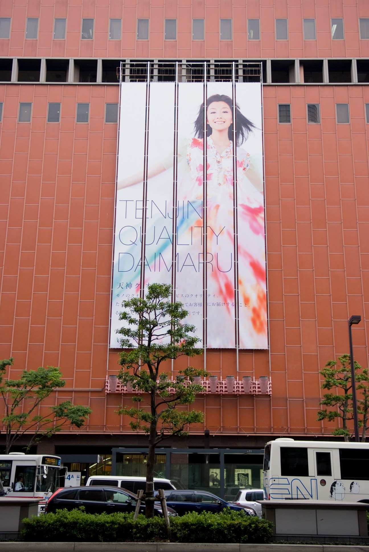 Large banner advertisement on red brick building facade for Tenjin Quality Daimaru department store