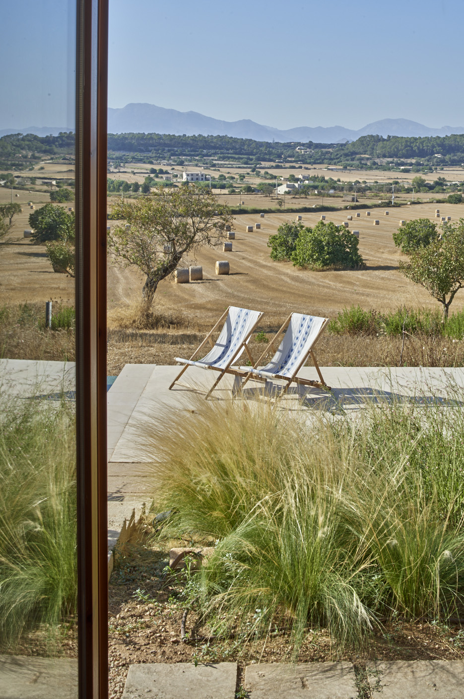 View through glass doors of terrace with two lounge chairs overlooking harvested fields and mountains