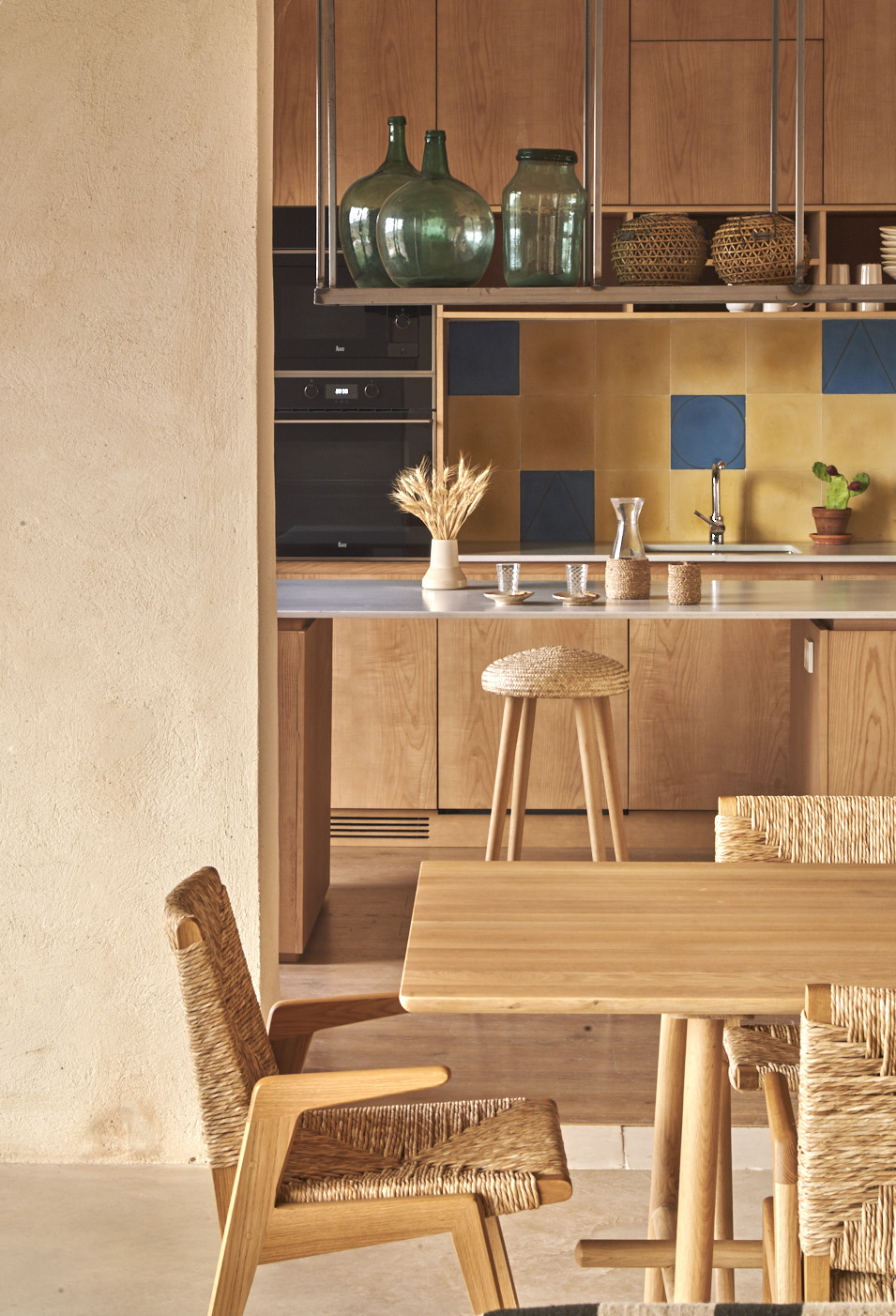Kitchen with wood cabinets, colorful tile backsplash, woven bar stools and dining table