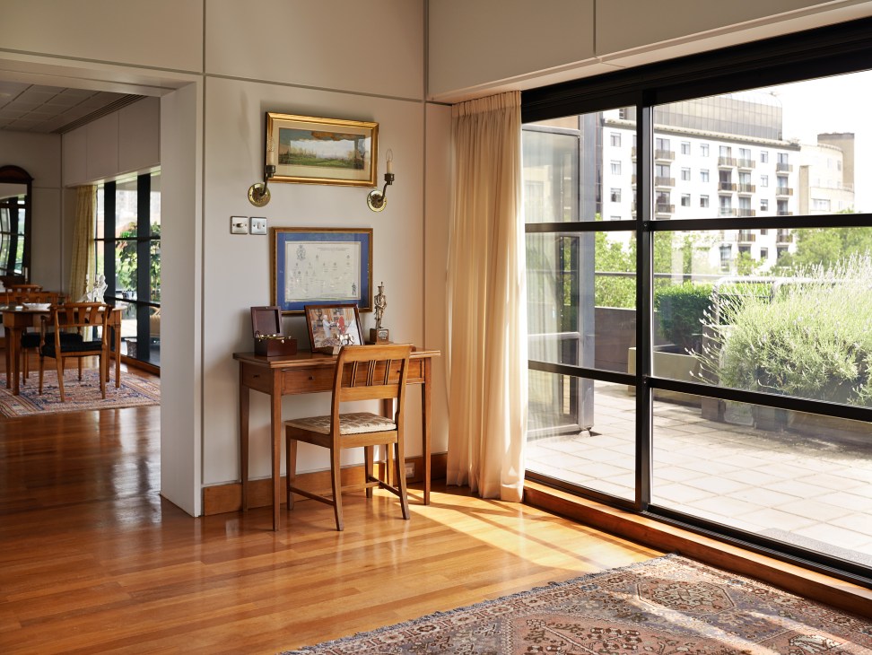 Danish embassy reception room with wooden desk, framed artwork, polished floors, and large sliding glass doors opening to a terrace.