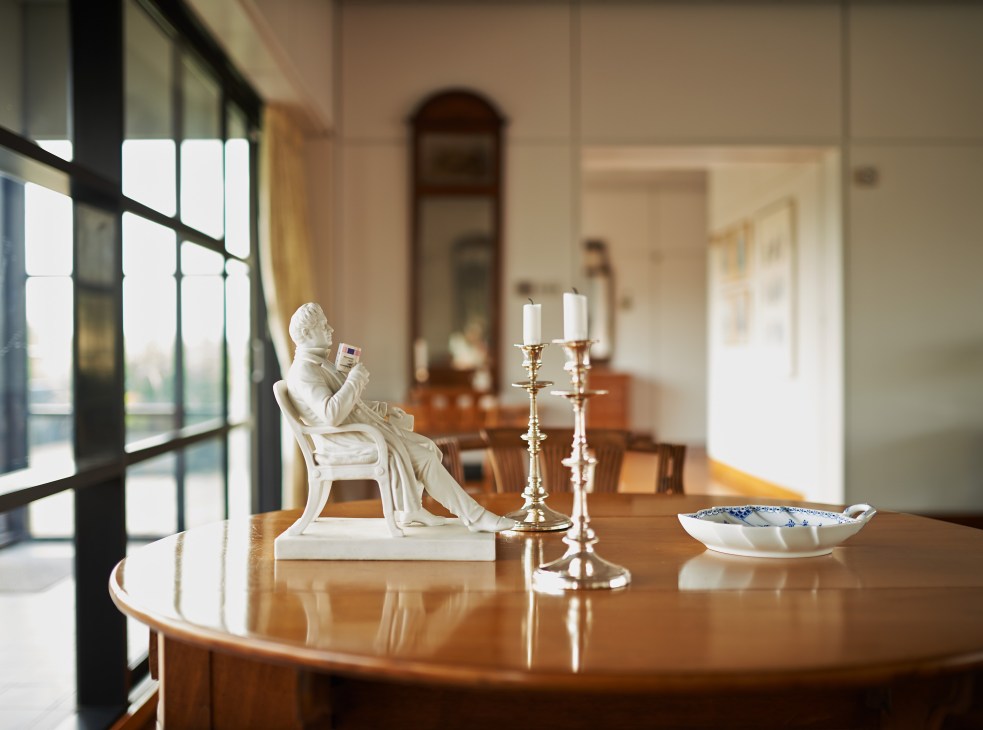 White porcelain figurine of playwright Adam Oehlenschläger on an oval dining table with candelabras and decorative objects.