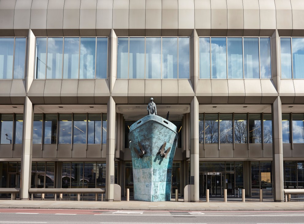 Bronze ship's-prow sculpture with a figure standing atop at the IMO headquarters entrance.