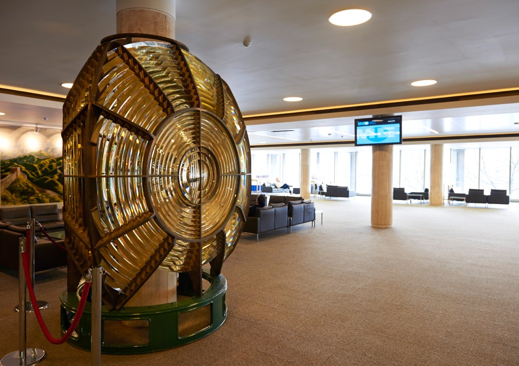 Salvaged brass lighthouse optic lens installed around a pillar in the IMO lobby