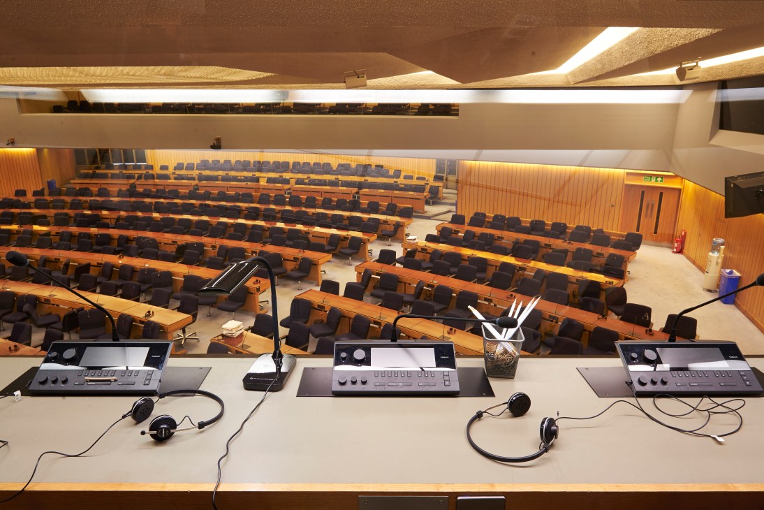 IMO plenary hall with rows of wooden delegate seating, translation headsets, and interpretation booths with equipment.