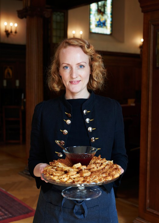 Woman in dark blazer holding plate of heart-shaped waffles in church interior