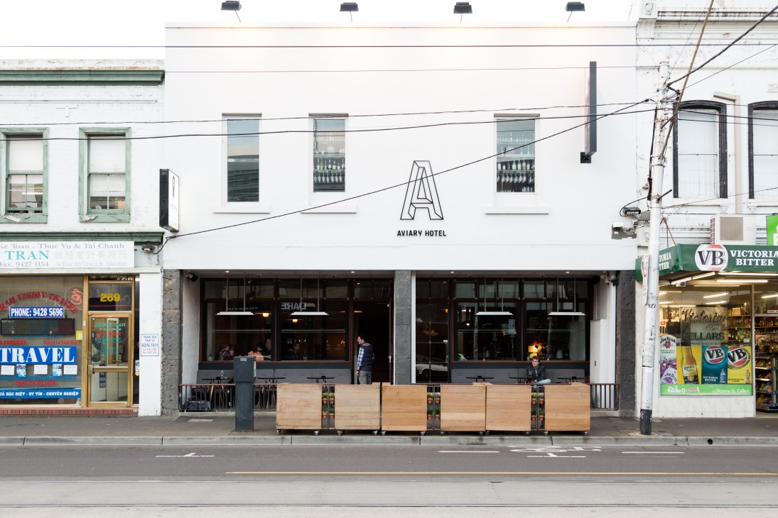 Aviary Hotel storefront with white facade, outdoor seating, and signage on a Melbourne street.