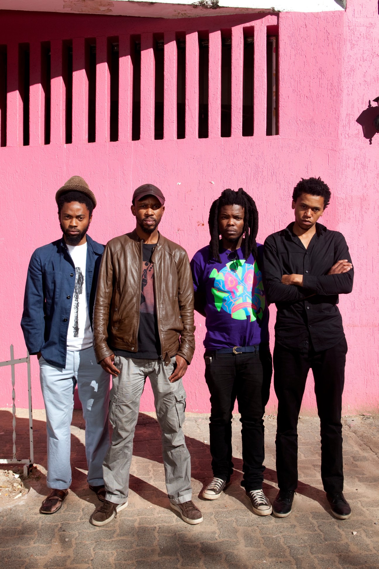Four members of South African rock band BLK JKS standing against a bright pink wall in Johannesburg.