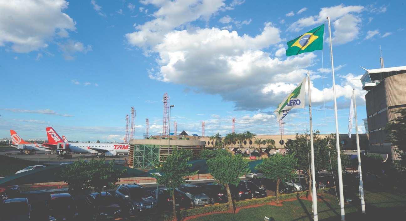 Brazilian airport terminal with TAM airline aircraft, Brazilian flag, and modernization infrastructure under clear sky.