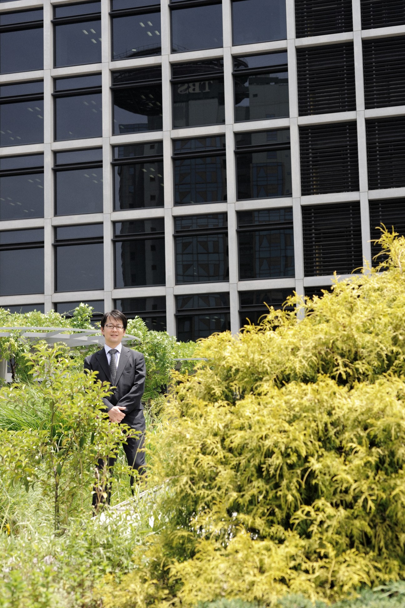 Yoriyuki Yamada in business suit standing among green plants on Kajima's rooftop garden in Tokyo.