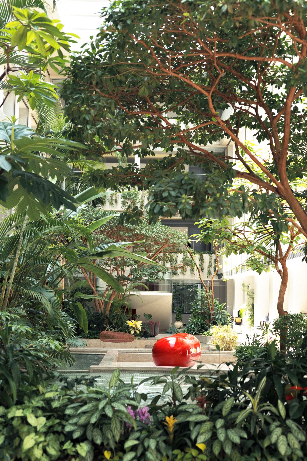 Lush green plants and trees surround a red spherical sculpture in Kajima's office atrium courtyard.