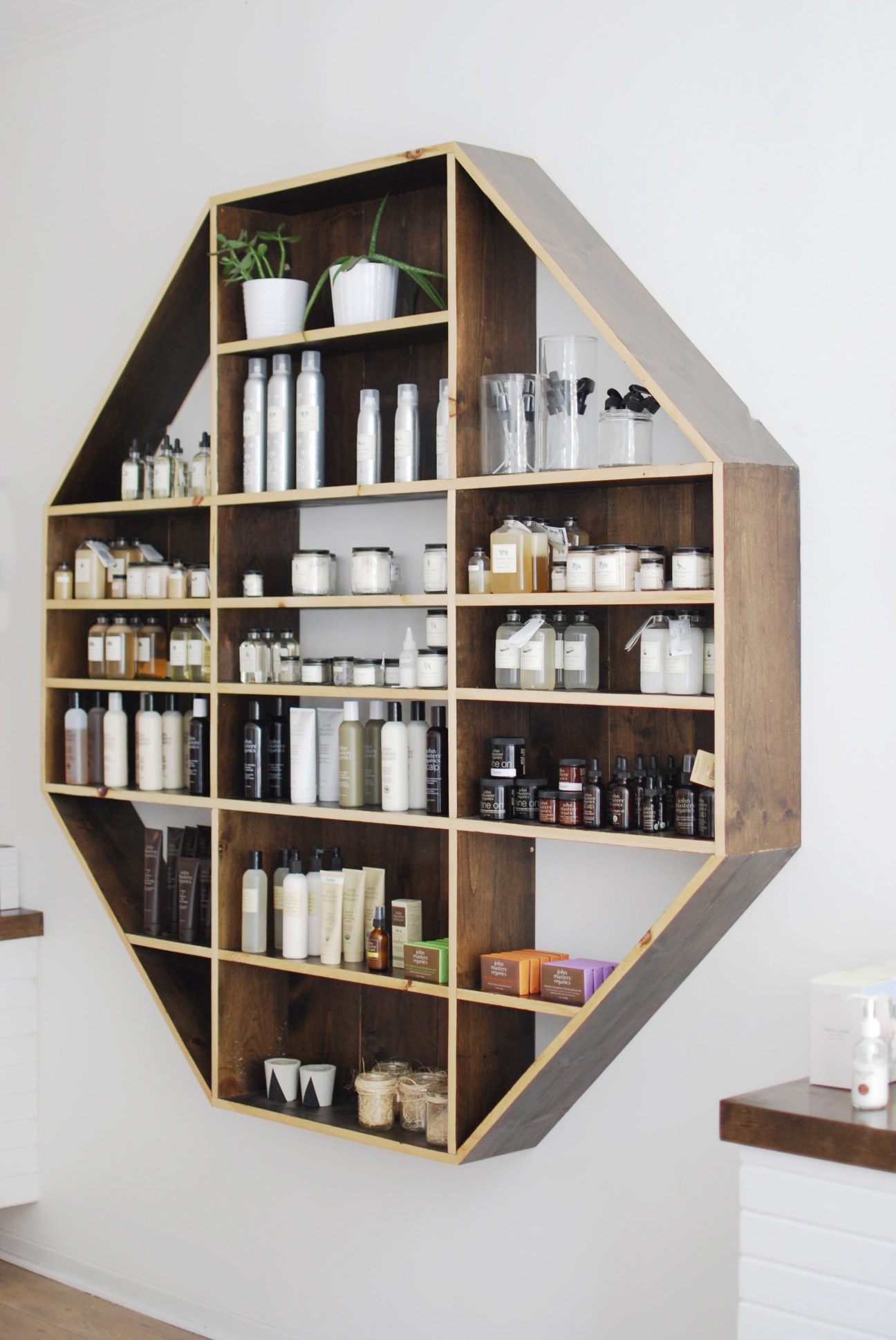 Hexagonal wooden shelving unit with brass frame displaying skincare products and toiletries in white and amber bottles.