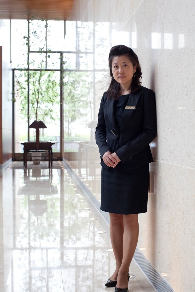 Senior manager Choi Bo-hyun stands in a modern corridor at Jack Nicklaus Golf Club Korea wearing a black blazer.