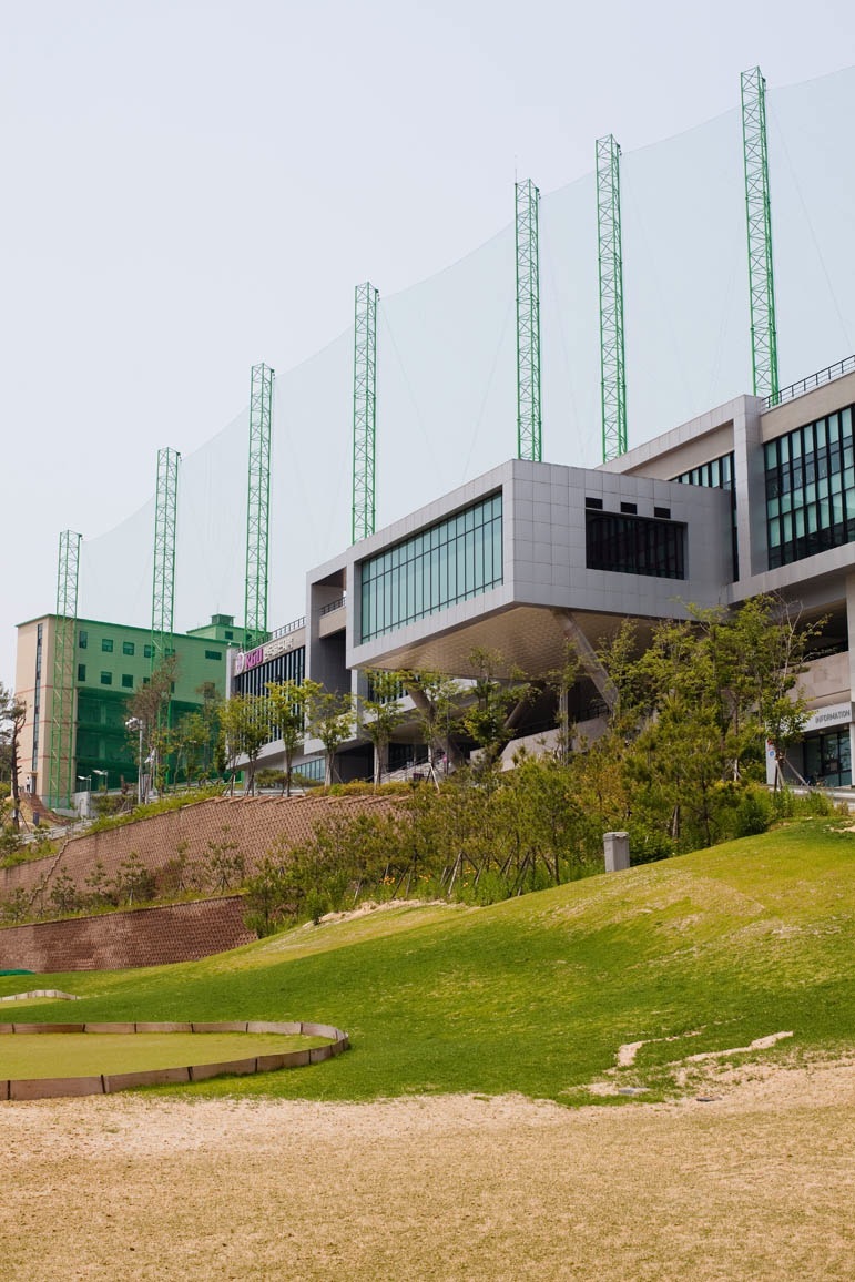Korea Golf University driving range with modern multi-level practice facility and green metal towers against landscaped grounds.