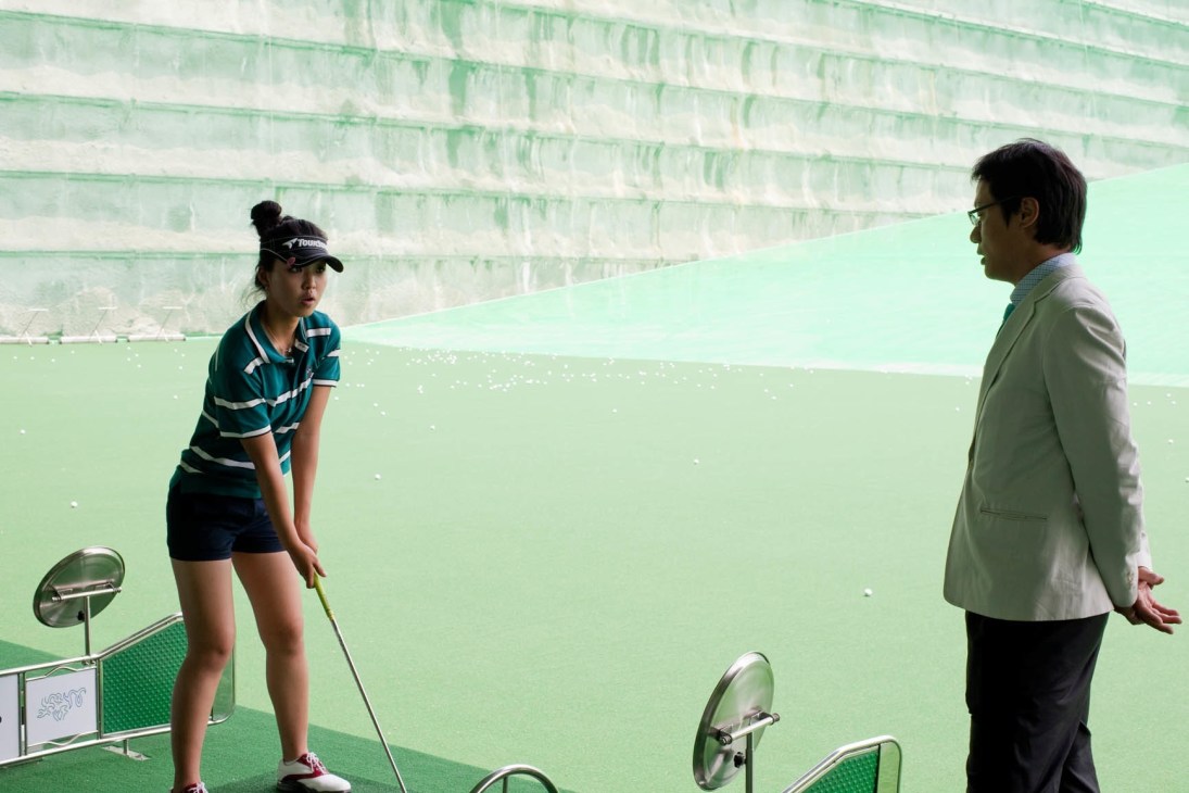 Young female golfer Kim Ga-yeong practices her swing while her coach observes at Korea Golf University.