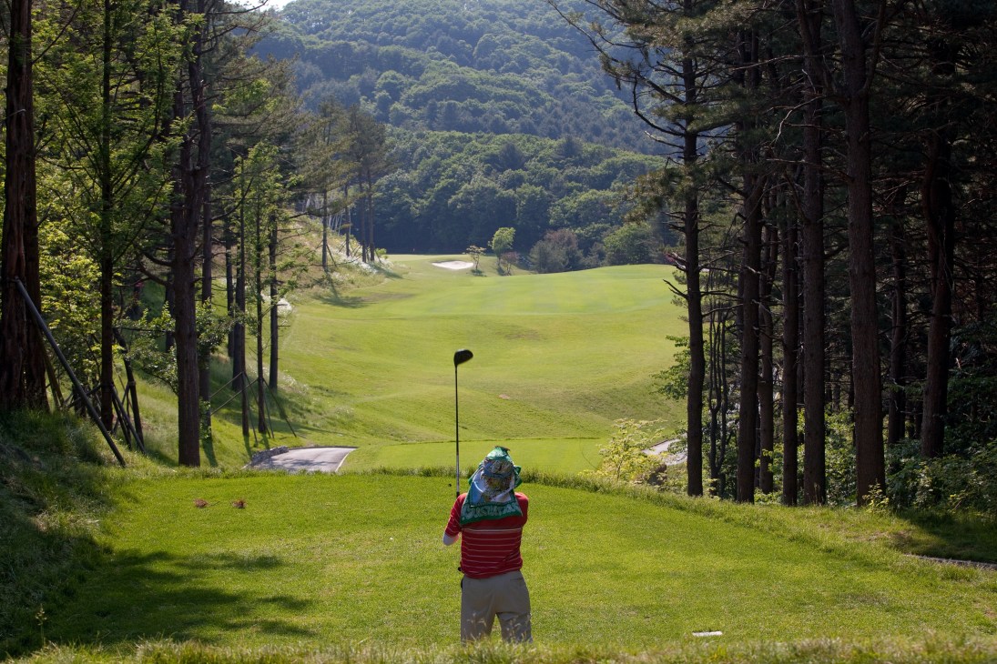Golfer taking a tee shot on a scenic course surrounded by forested mountains at Ananti golf club.
