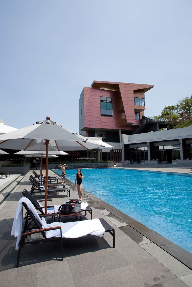 Modern red tower building overlooking swimming pool with loungers and umbrellas at Ananti golf club.