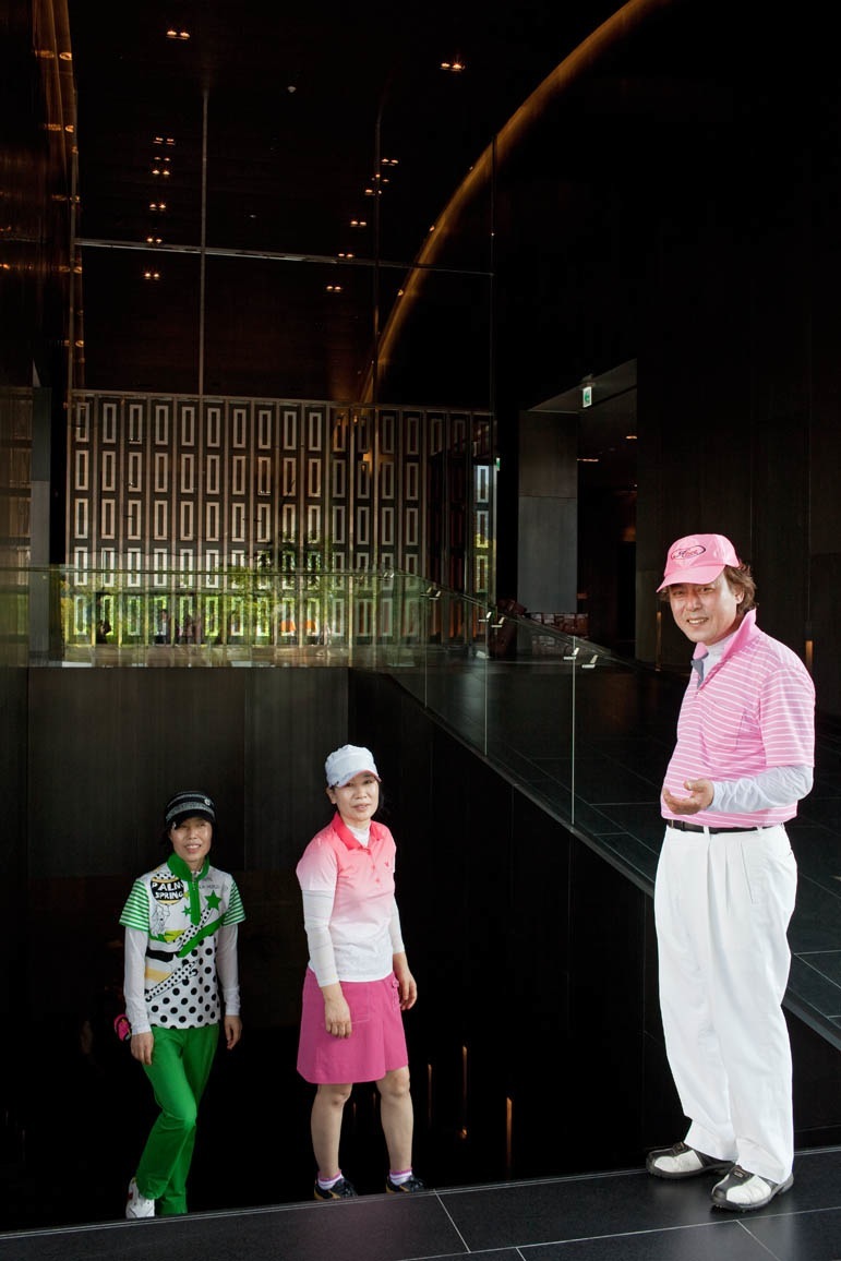 Three people in colorful golf attire standing in a modern dark interior space with illuminated signage.