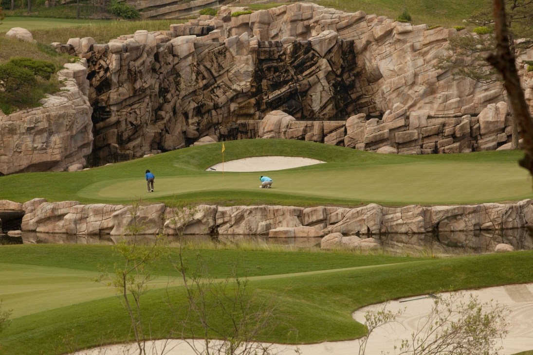 Two golfers on a pristine green with dramatic rocky outcrops at Haesley Nine Bridges Golf Club.
