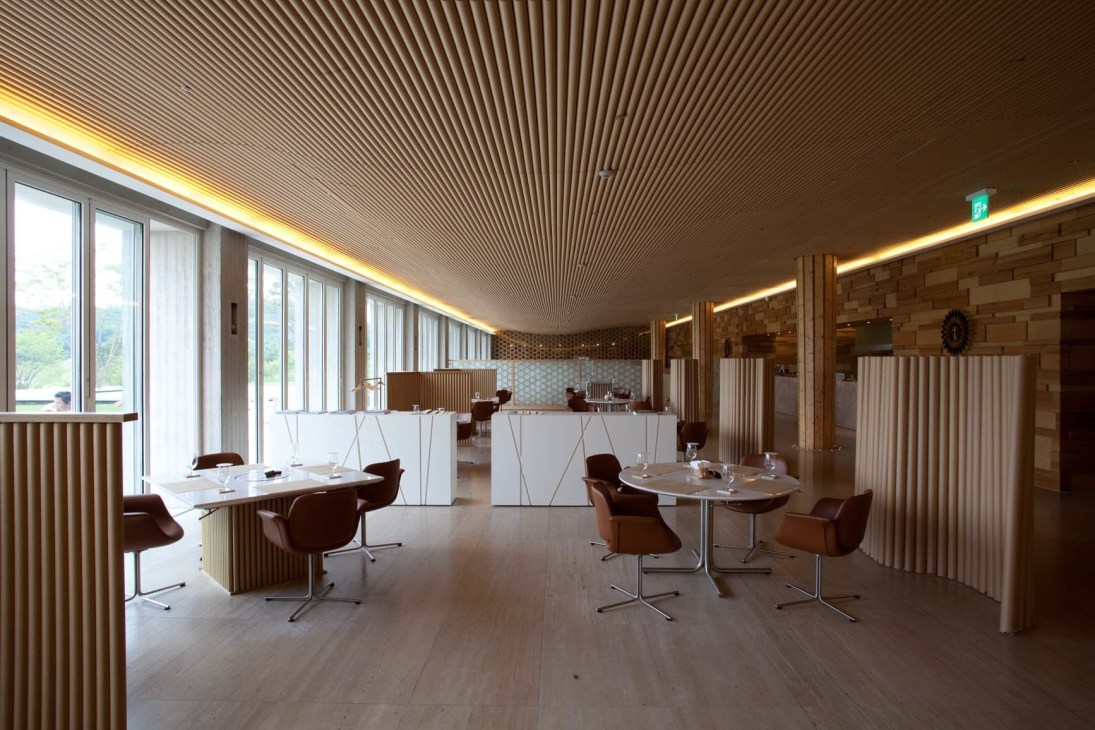 Interior of Haesley Golf Club showing Shigeru Ban's distinctive paper-tube ribbed ceiling with warm lighting and modern furnishings.