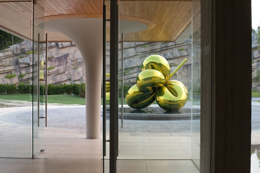 A shiny golden Jeff Koons sculpture of tulips displayed inside a modern glass-walled space at Haesley Golf Club.