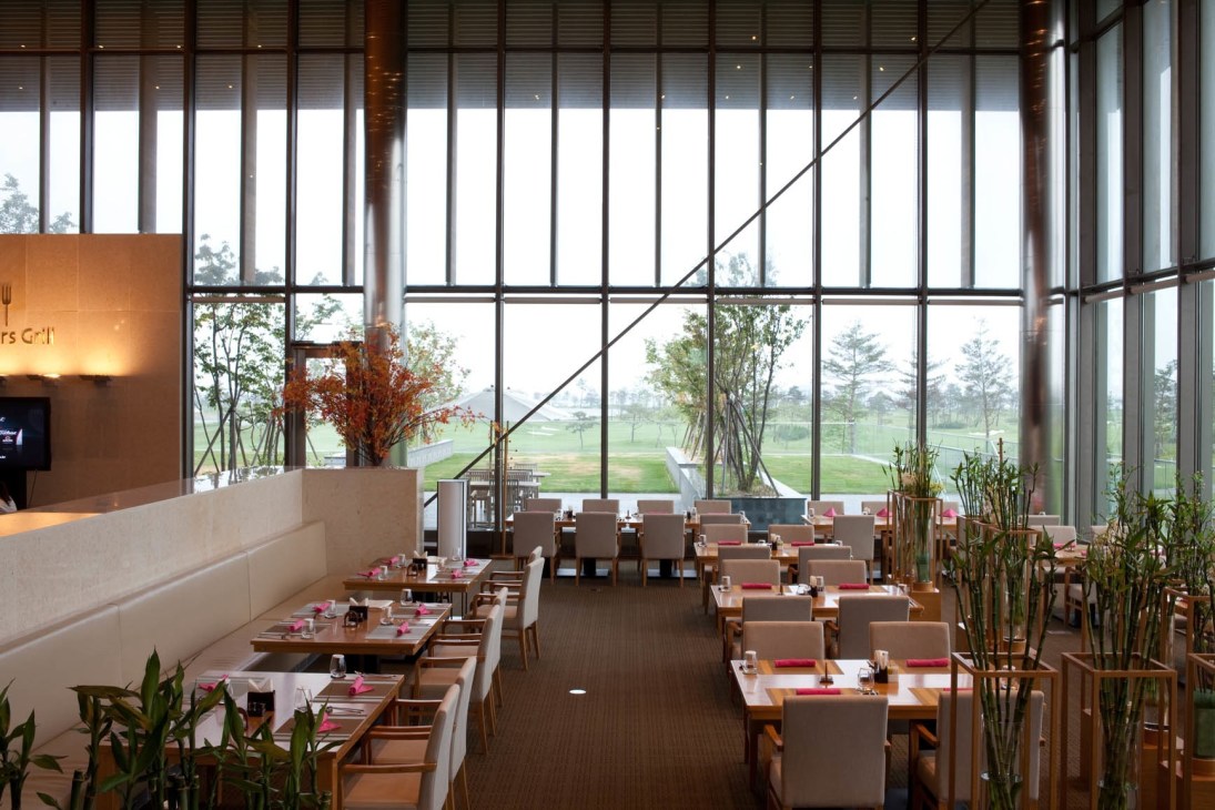 Modern restaurant interior with floor-to-ceiling windows overlooking a golf course.