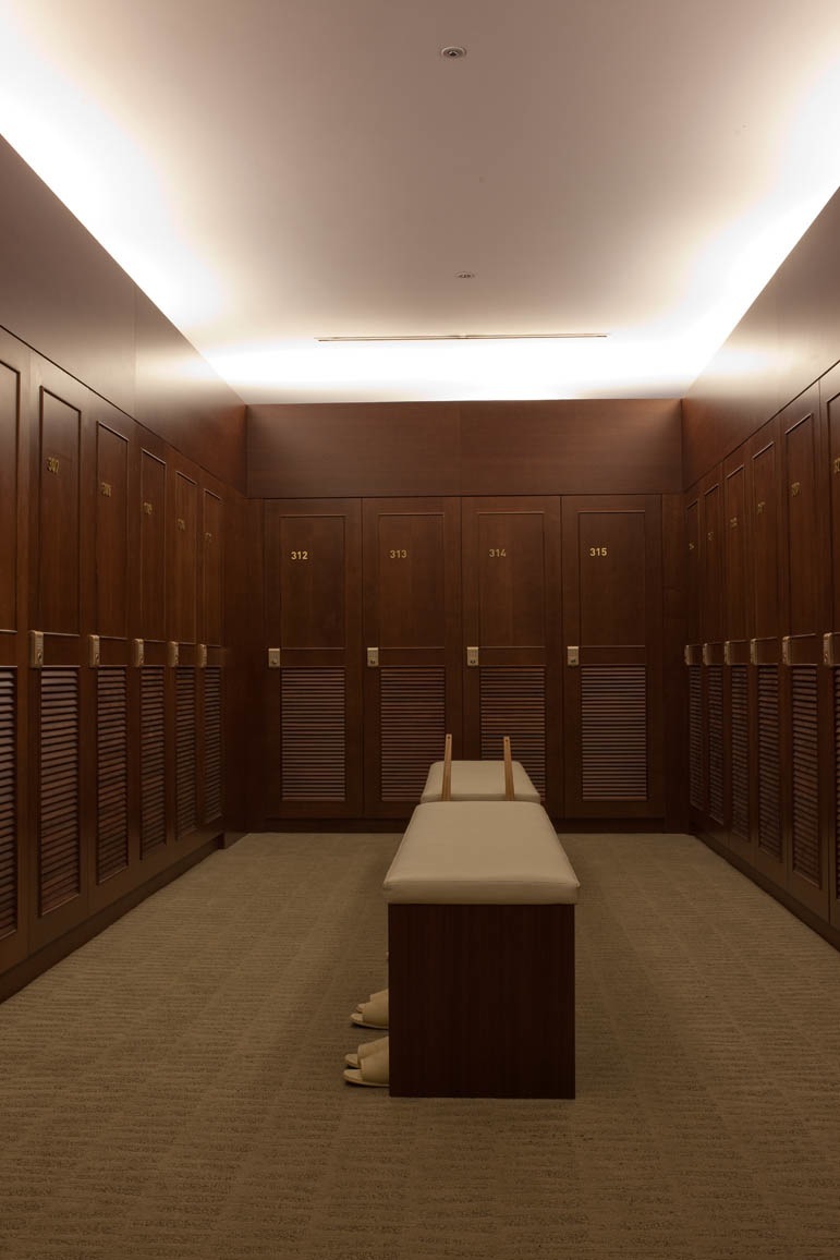 A luxurious changing room with dark wood lockers numbered 312-315 and cream-colored seating along a center bench.