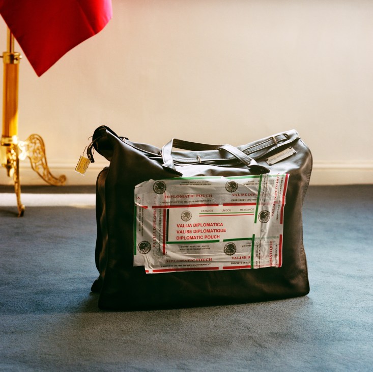 Mexican diplomatic pouches labeled with red and green text inside a black leather bag next to a flagpole with red flag.
