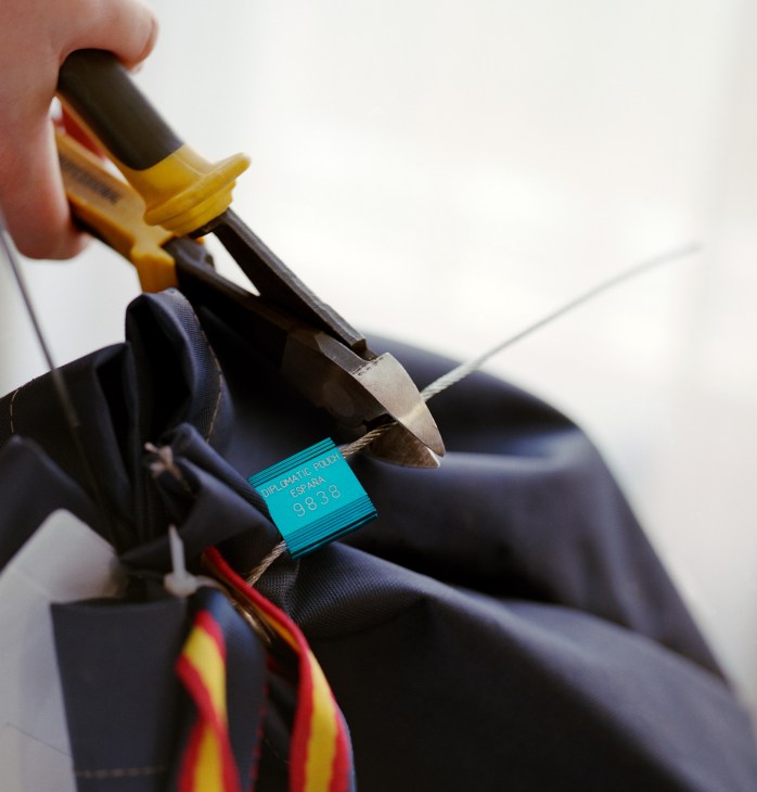 Heavy clippers cutting excess wire from a sealed Spanish diplomatic pouch lock.