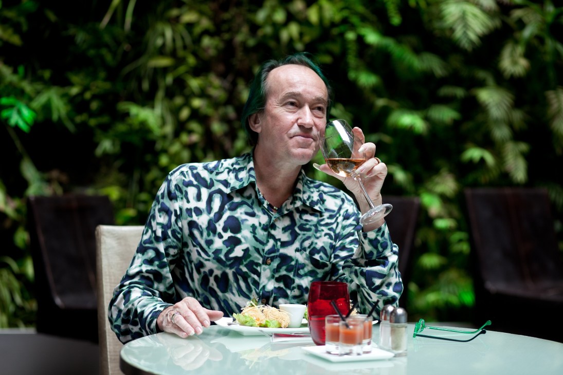 Patrick Blanc holds a glass of rosé while seated at a table in front of a lush vertical garden at Pershing Hall.