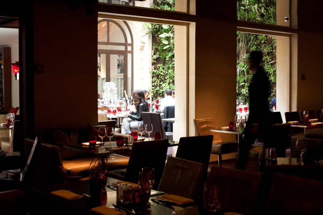 Pershing Hall restaurant interior with vertical garden wall visible through windows and diners seated at tables.