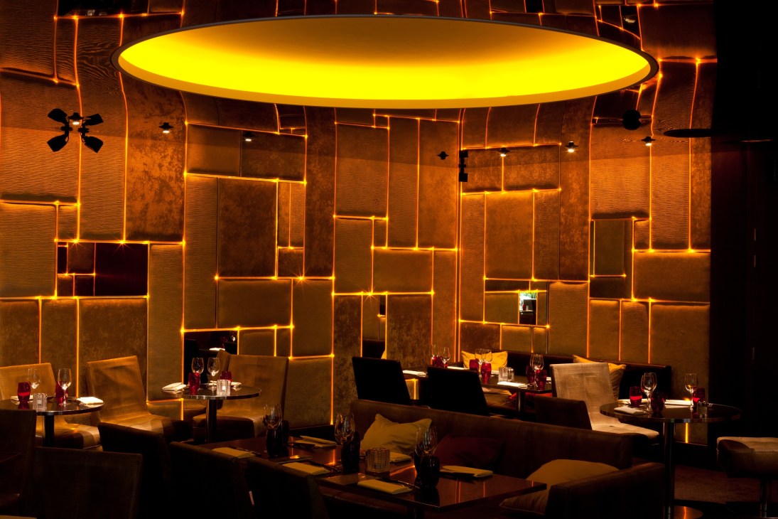 Illuminated lounge seating area with gold-framed wall panels and circular ceiling light at Pershing Hall restaurant.