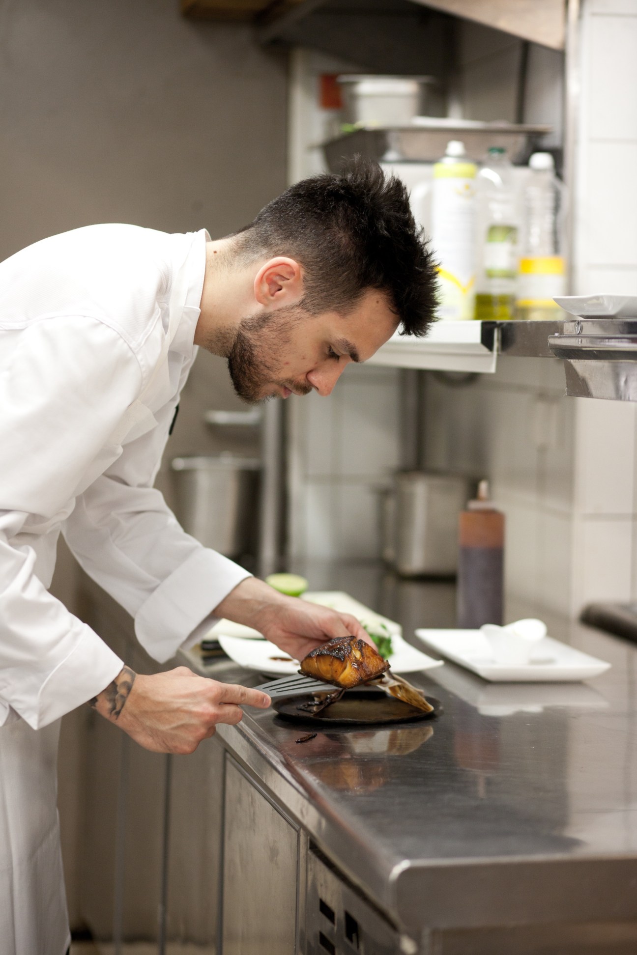 Chef in white chef's coat plating caramelised black cod in a professional kitchen.